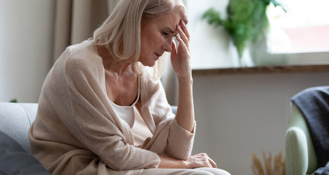 Stressed woman sitting on couch, showing signs of menopause anxiety.