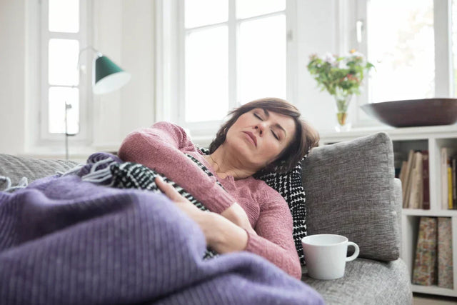 Middle-aged woman experiencing menopause fatigue resting on a couch.