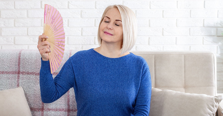 Middle-aged woman experiencing premenopause cooling off with a hand fan.